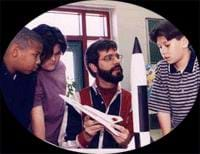 Photo of three kids and an adult man with rocket models.