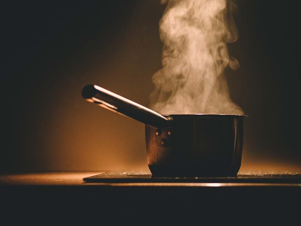 A dark image of a pot with a handle and steam coming off it the top. 