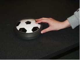 A photograph shows a hand pushing a hover puck with a soccer ball design.