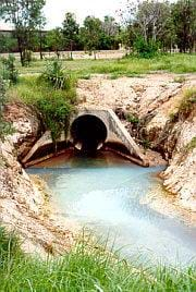 Photo shows a big, buried concrete pipe opening out into a gully. 