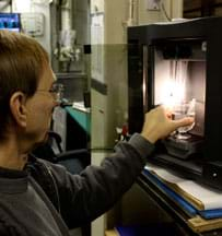 Photo shows a man putting a beaker and test tube of clear fluids into a black, box-shaped desktop appliance.