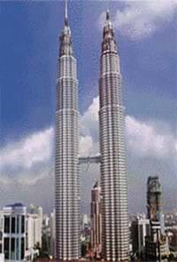 A photograph shows two side-by-side thin skyscrapers, connected by a mid-way horizontal bridge.