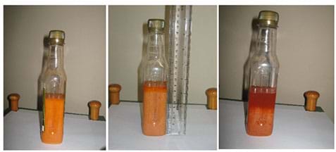 Three photographs show the same tall, capped clear bottle that contains a blood model composed of equal volumes of V8 drink with 1% solution of petroleum jelly in olive oil. From left to right, the mixture’s particles are settling to the bottom, leaving clearer orange liquid at the top.