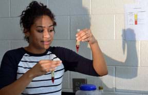 A photograph shows a high school junior girl looking at test tubes in her hands, examining the centrifuged blood model she created from beet juice, petroleum jelly and olive oil.