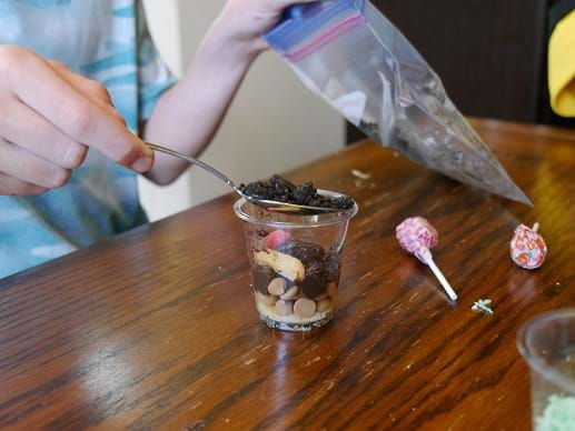 A picture of hand spooning crushed Oreos in the cup.