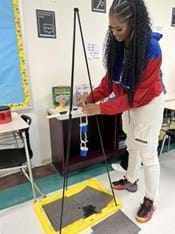 A photo showing a teacher attaching her shower clock prototype to a stand prior to testing. A photo showing a teacher attaching her shower clock prototype to a stand prior to testing.