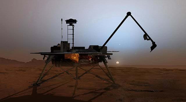 A picture showing an artist's rendering of the Phoenix Mars Lander sitting on the rust-colored Martian surface at twilight. The lander, supported by three metallic legs, has a distinctively long, thin robotic arm extended upward and to the right, ready for scooping or analysis. In the background, a hazy sky meets the horizon, with the faint disk of the sun or a moon visible just above the surface. The scene is dimly lit, casting deep shadows from the lander and its arm. A picture showing an artist's rendering of the Phoenix Mars Lander sitting on the rust-colored Martian surface at twilight. The lander, supported by three metallic legs, has a distinctively long, thin robotic arm extended upward and to the right, ready for scooping or analysis. In the background, a hazy sky meets the horizon, with the faint disk of the sun or a moon visible just above the surface. The scene is dimly lit, casting deep shadows from the lander and its arm.