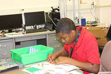 A photograph shows a boy working at a table, assembling a small-sized car prototype from a boxed kit.