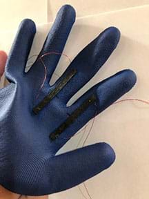 A blue rubber glove that has two black strips on the first two fingers. The black strips have a wire coming from each end of them. 