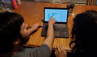 A picture of two students working on the activity. One student is pointing at the block code on the Tinkercad site to discuss steps with his partner. 