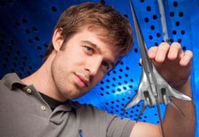 A man holds and examines a small model of a sleek silver airplane.