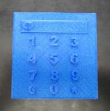 A photograph shows a thin blue square plastic piece that looks like a calculator. Raised on the surface is a short and wide rectangle with the numbers 1-9 below in three rows and the characters "@ 0 *" on the fourth row. 