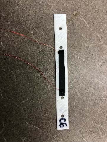 A long white strip of rubber material with a smaller black strip of rubber attached to the top. The small black strip has a small wire attached to both ends.