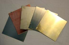 A photograph shows five squares of thin metal alloy materials of various metallic colors: grays, bronze, silver and gold. 