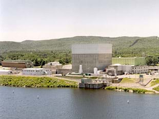 A photograph shows nuclear power plant, which looks like a compound of assorted short and tall buildings along the bank of a river.