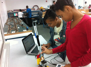 Photo shows two students working on robotics. They are learning about the properties of robots that are needed to break through the door.