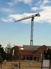 Photo shows a tall vertical truss structure high above a building, with a horizontal truss structure at its top.