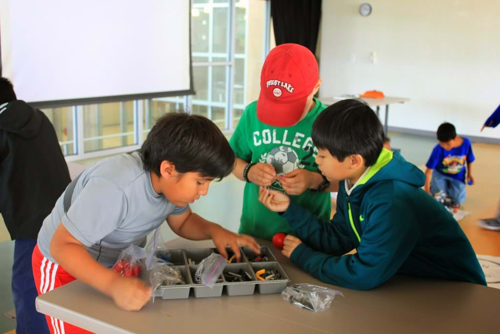 Three boys are gathered around picking up LEGO pieces.