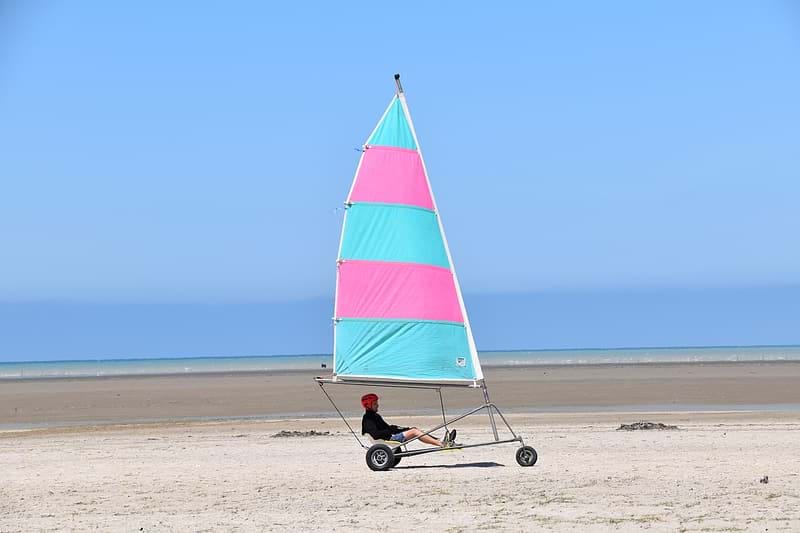 A man riding on a pink and blue vehicle that transforms the (kinetic) energy in wind to usable energy for vehicular motion.