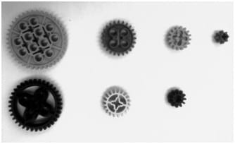 A black and white photograph shows seven round plastic disks of different sizes, each with toothed edges and various interior cutouts.