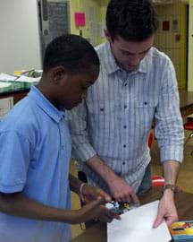 Photo shows a sixth-grade student and a GK-12 fellow (a college engineering student) at a table with a hand-held device and a piece of paper.