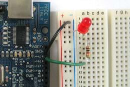 A photograph shows an Arduino microcontroller connected to a red LED using two jumper wires, a breadboard and a resistor.