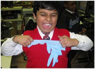 A photograph shows a young boy using both hands to stretch and rip apart with all his might a light blue plastic glove.
