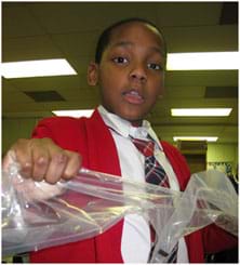 A photograph shows a young boy with a tight grasp on a piece of clear plastic sheeting as he stretches it apart.