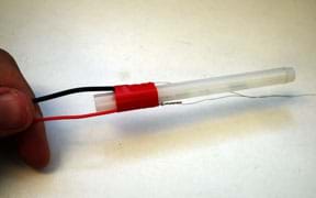 A photograph shows red electrical tape applied to the solder joints to tape two wires to opposite long sides of a plastic cylinder.
