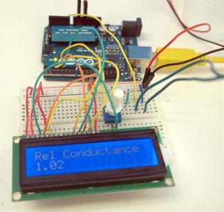 A photograph shows a microcontroller board connected by wires to a breadboard with many colored wires and some circuitry components as well as a LCD display that reads: Rel Conductance 1.02.