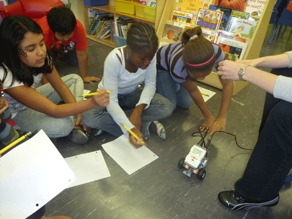 Photo shows four students sitting on the floor approximating the distance a robot travelled.