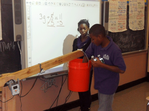 Photo shows two students moving objects from one bucket to another.