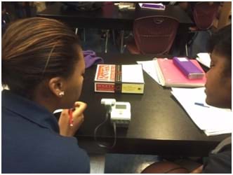 Photo shows two students at a table using an ultrasonic sensor to measure the distance to a book on the table.