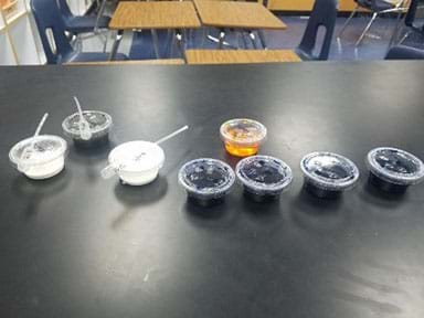 Eight solo cups filled with dye solutions and white solutions of nanoparticle samples.