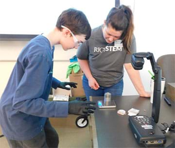 Teacher bent over a digital scale helping a student read the mass on the screen. 