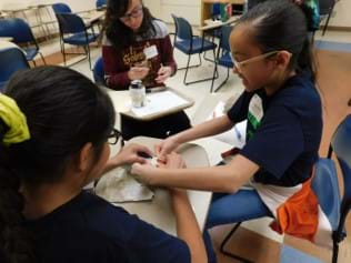 Students with hands-on building car safety feature out of paper and cardboard.