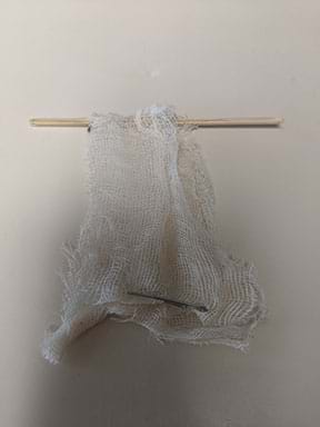 A photograph shows a piece of cloth wrapped over a wooden skewer. A paper clip is attached to the bottom of the cloth as weight.
