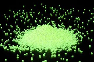 Particles glow green under a black light. The surroundings are completely black.
