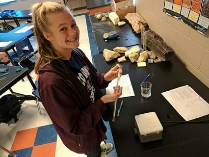 A smiling student is ready with a thermometer, beaker, and hotplate as she prepares mung bean seeds for heat treatment.