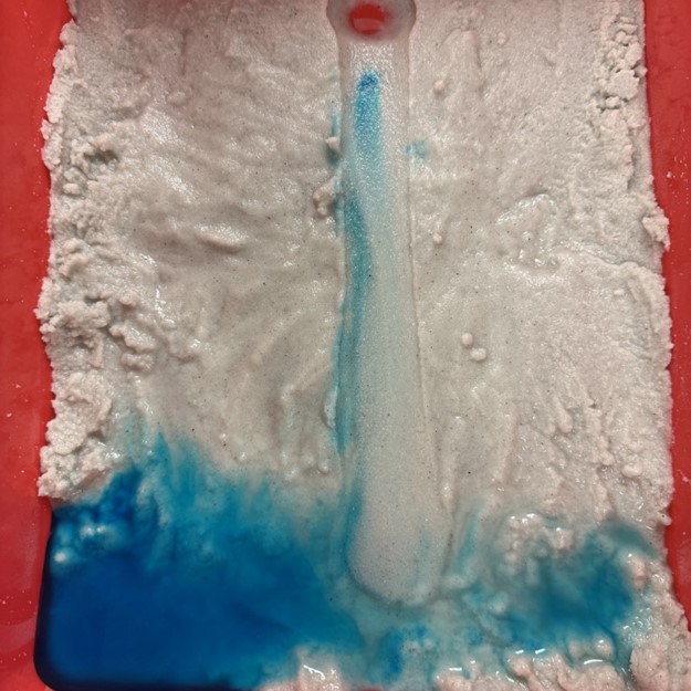 An image illustrating the movement of pollutants (represented by food coloring) as they travel downstream in a bayou. Some pollutants settle along the bayou's banks, while most disperse across the surrounding low-lying land areas.