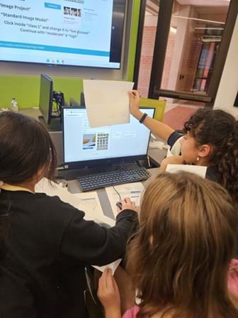 A photo showing three students working together in front of a computer screen. 