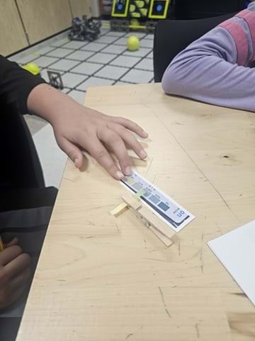 A photo showing a student comparing a test strip held in a clothespin against a color chart.