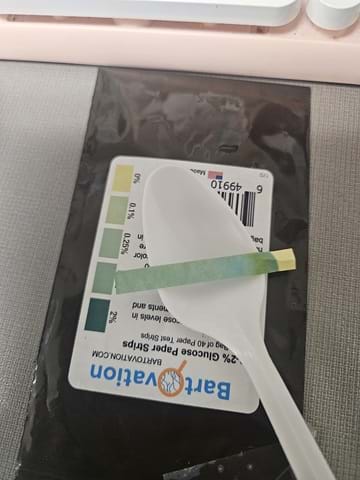 A photo showing a glucose testing strip on a plastic spoon that lies on top of the color strip. 