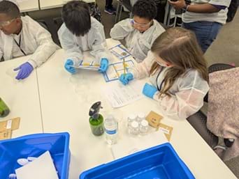 A photo of four students wearing personal protective equipment working on their project. 