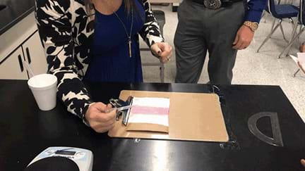 A woman’s arm with an eyedropper of liquid leans over a clipboard with a material showing a person testing the roll off angle.