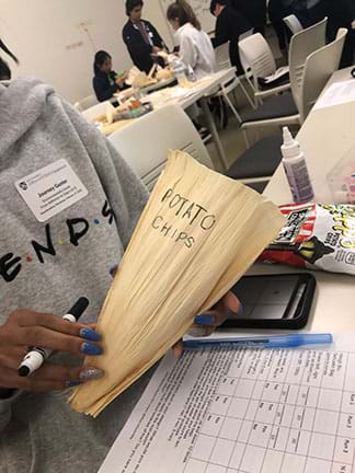 Image of a student holding a biodegradable bag design made out of a corn husk.