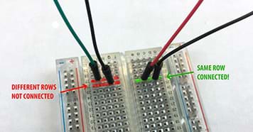 A photograph shows a breadboard with four wires plugged into it. The two wires on the left are in different rows and so are not connected. The two wires on the right are in the same row and so are connected.