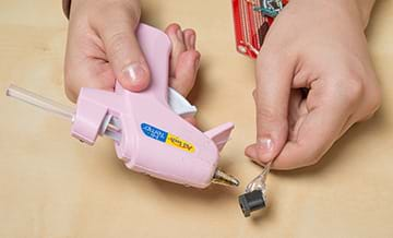 A photograph shows two hands hot gluing the wires of a barrel jack.