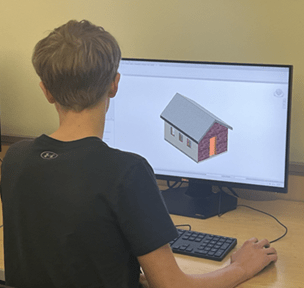 A photo of a student sitting at a computer station with a model of a small building on the screen. 
