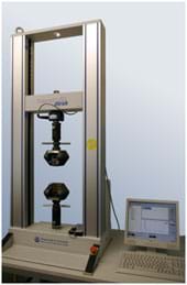 A photograph shows a desktop machine shaped like the frame of a tall open window with two sensors positioned from above and below that squeeze material placed between them. The force of the squeeze and the response of the material are recorded by a computer nearby. A photograph shows a desktop machine shaped like the frame of a tall open window with two sensors positioned from above and below that squeeze material placed between them. The force of the squeeze and the response of the material are recorded by a computer nearby.
